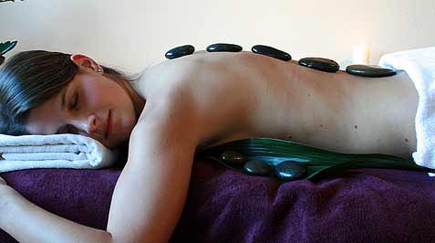 das Bild zeigt eine Patientin, welche die heissen Steine einer Hot-Stone-Therapie auf dem Rücken liegen hat